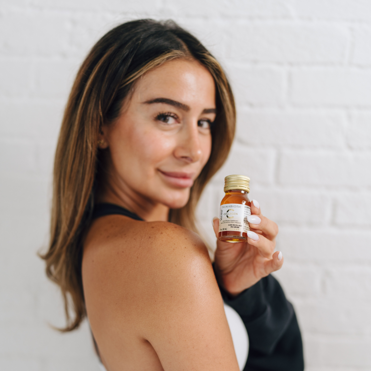 donna con capelli castani tiene in mano un flaconcino di Primabiotic Collagen 10000 mg davanti a una parete bianca