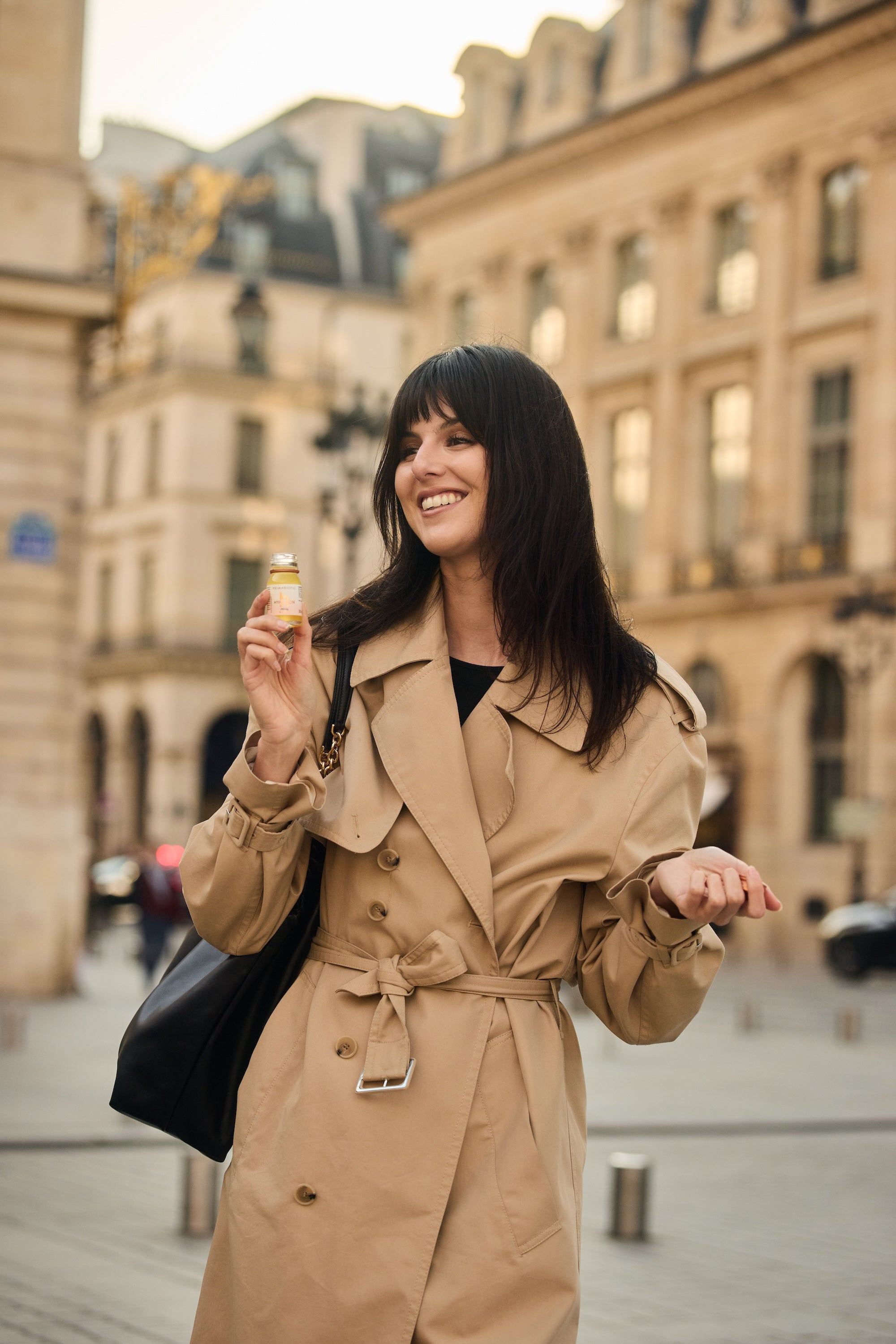 donna con impermeabile beige sorride tenendo un flaconcino di Primabiotic Hyaluron