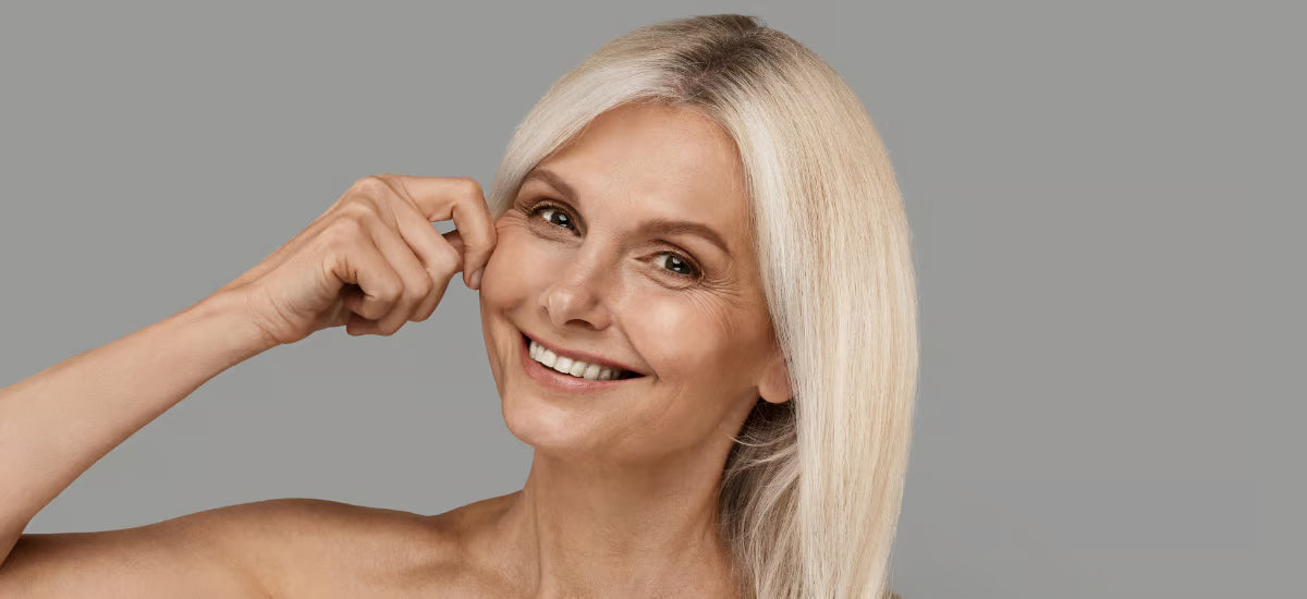 Donna sorridente dai capelli grigi che pizzica la guancia, mostrando pelle tonica dopo la supplementazione di collagene Primabiotic.
