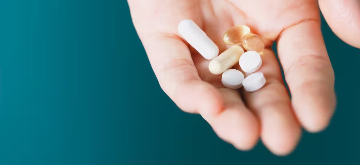 Una mano con una manciata di medicinali su uno sfondo verde