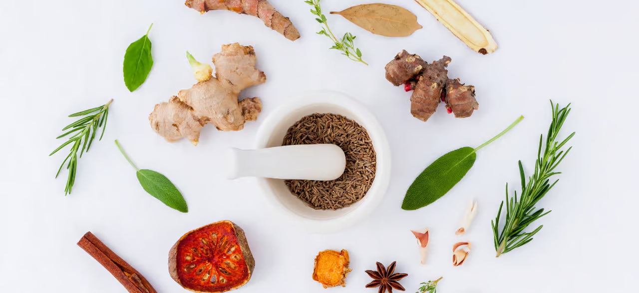 Un mortaio con dei semi al centro e intorno a esso vari ortaggi e spezie, ad esempio zenzero, rosmarino, peperoncini.