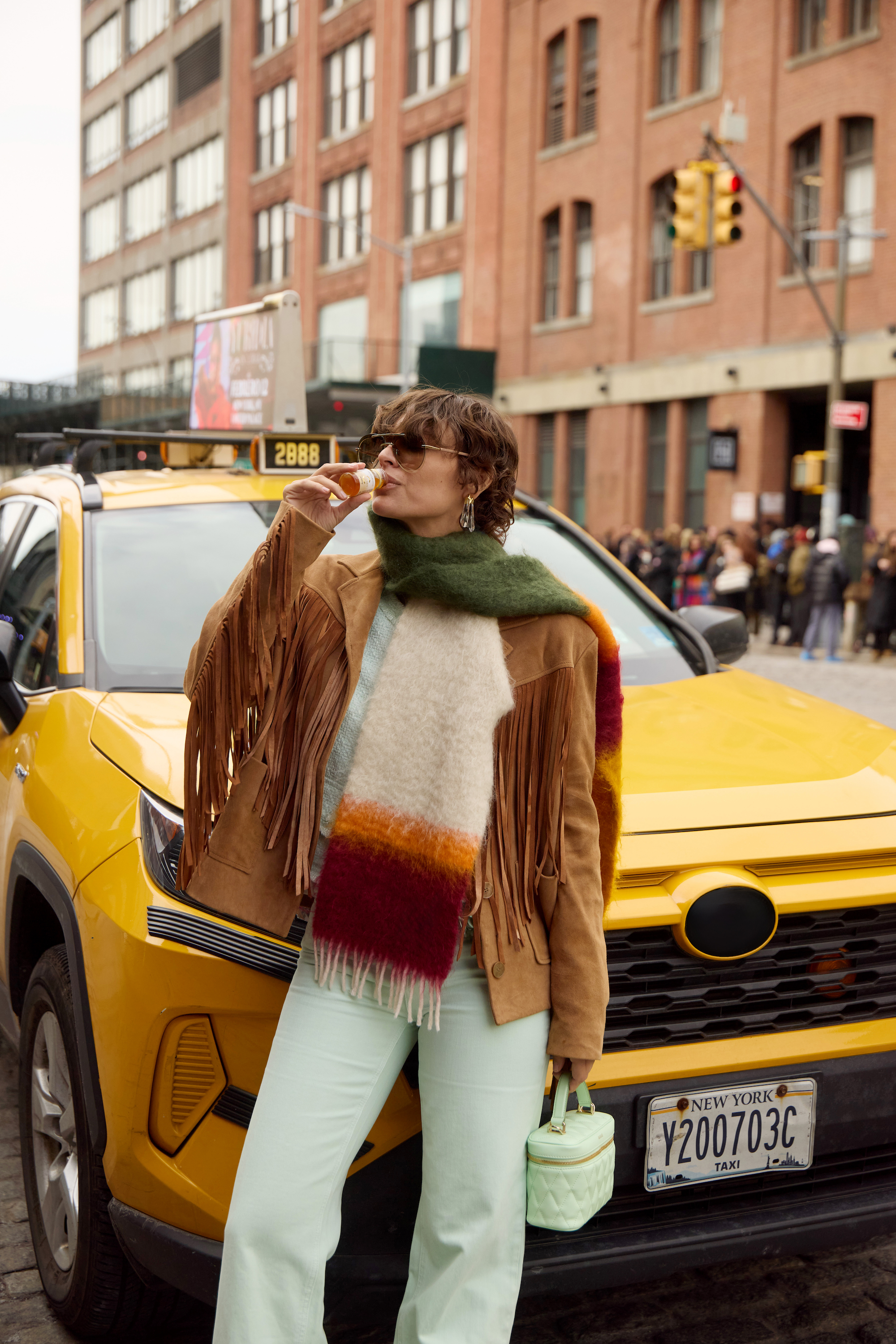 donna con occhiali da sole beve un flaconcino di Primabiotic davanti a un taxi giallo a New York