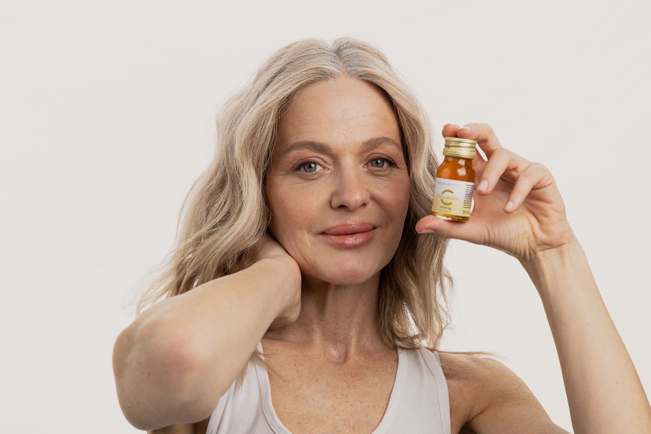 donna matura con flaconcino Primabiotic Collagen 10000 mg 30 ml in mano davanti a sfondo chiaro