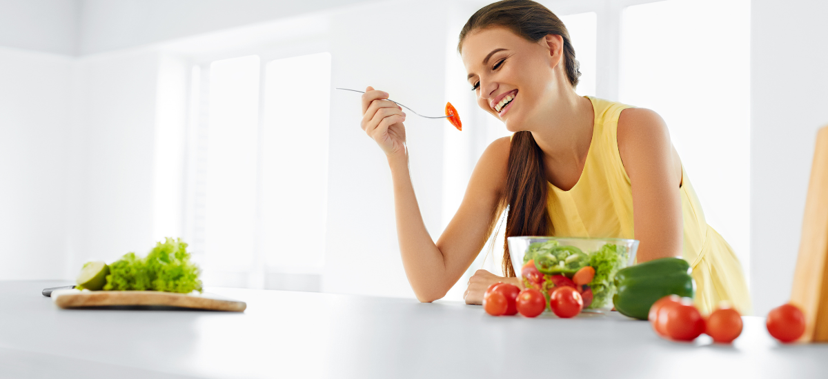 Donna sorridente che mangia un'insalata in cucina.